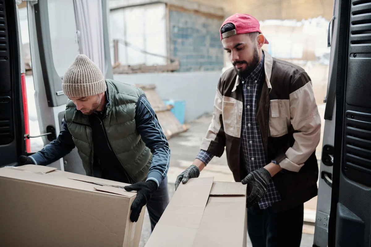 Two workers handling cardboard cartons beside a delivery van.