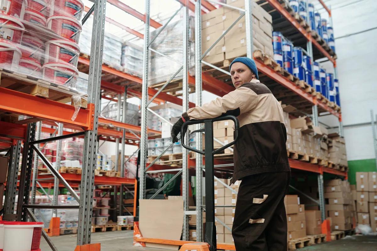 Warehouse worker moving a pallet jack between storage racks.