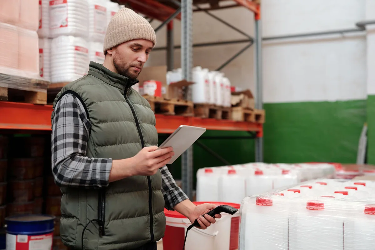 Warehouse worker using a tablet beside stored goods.